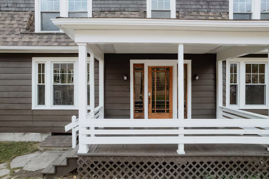 A covered front porch with white railings and a warm wood-toned door against charcoal siding