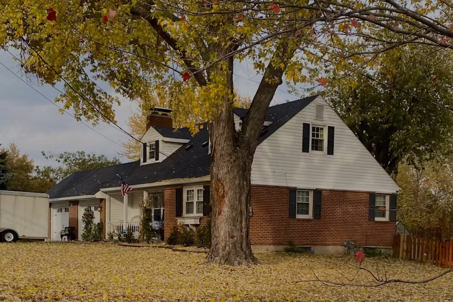 A brick and white-trim home framed by an autumn tree with fallen leaves on the lawn — Westland, Michigan